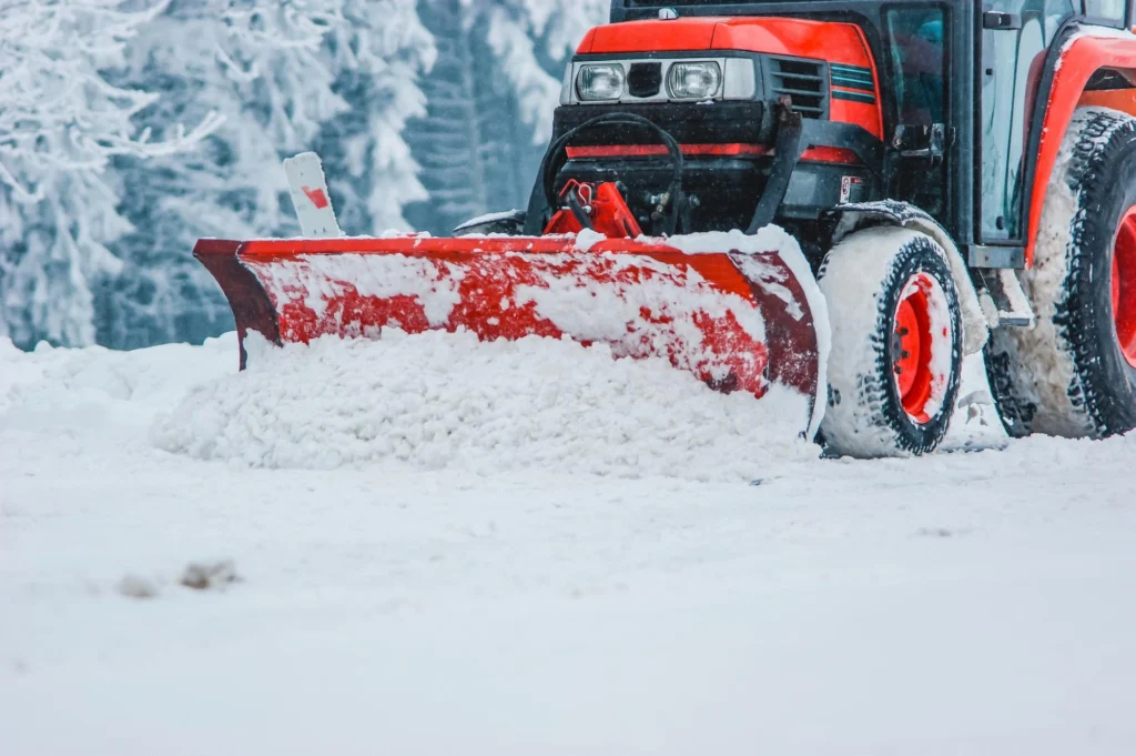 Worker using a snow blower to clear a driveway during winter near residential homes.