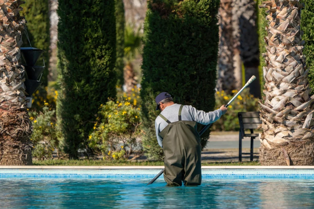 Two pool maintenance technicians standing beside a swimming pool and service van, holding cleaning equipment and tools.