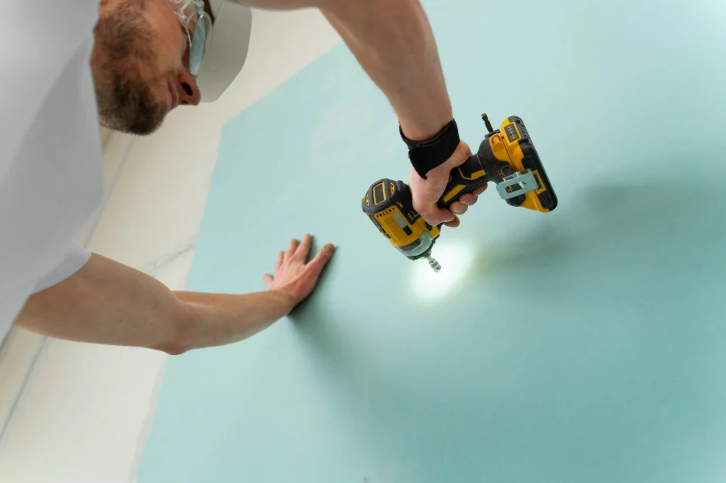 Construction worker installing drywall panels on a wall frame at a building site
