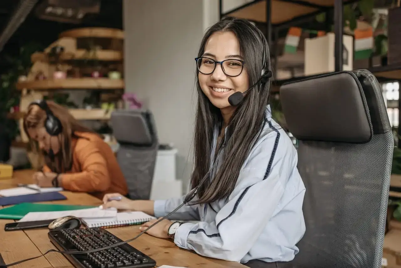 Smiling woman in a modern office, engaged in collaborative work with team members.